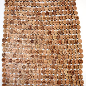 Puede incluir: Una colecci&oacute;n de m&aacute;s de 200 fichas redondas de madera con varios dise&ntilde;os y textos. Las fichas est&aacute;n dispuestas en una cuadr&iacute;cula y presentan una variedad de temas, que incluyen bares, restaurantes y negocios locales. Algunas de las fichas tienen texto como "Bebida gratis", "Una bebida gratis", "Buen trabajo" y "Hora feliz".