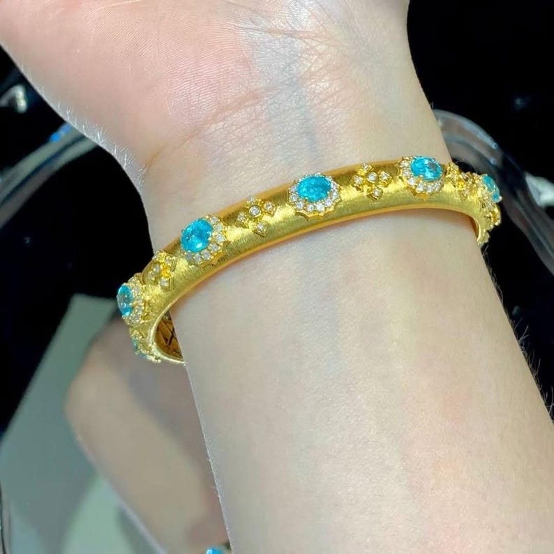 May include: A gold bangle bracelet with a textured surface and a row of oval-shaped turquoise gemstones set in a diamond halo.