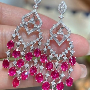 May include: Elegant chandelier earrings featuring a cascade of oval-cut, vibrant pink gemstones. The earrings have a diamond-encrusted, openwork design with a teardrop-shaped top and a diamond-studded post. The earrings are made of silver or white gold.