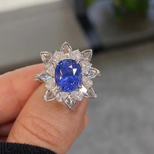 May include: A ring with a large blue sapphire surrounded by smaller diamonds in a flower-shaped setting.