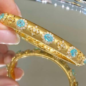 May include: A gold bangle bracelet with a delicate design featuring alternating blue gemstones and small diamonds.