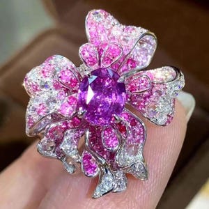 May include: A pink and white jeweled ring with a large purple gemstone in the center, shaped like a bow.