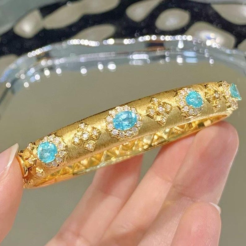 May include: A gold bangle bracelet with a brushed finish and a row of oval-shaped turquoise gemstones set in a diamond halo.