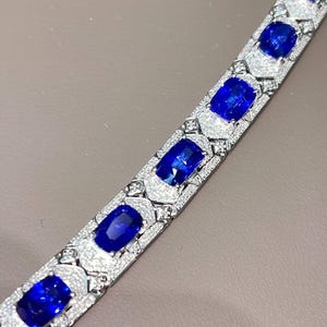May include: A silver bracelet featuring large, oval-cut, deep blue gemstones set in a pave diamond design. The bracelet's links are adorned with smaller diamonds, creating a sparkling, luxurious accessory.