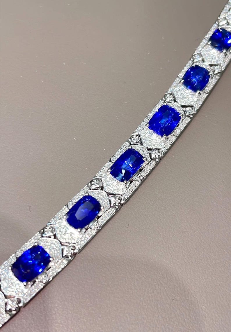 May include: A silver bracelet featuring large, oval-cut, deep blue gemstones set in a pave diamond design. The bracelet's links are adorned with smaller diamonds, creating a sparkling, luxurious accessory.