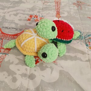 May include: Two crocheted turtle plushies, one with a lemon shell and the other with a watermelon shell. The turtles are green with black eyes and are stacked on top of each other. The text "Syd's Tangled Creations" is visible in the background.