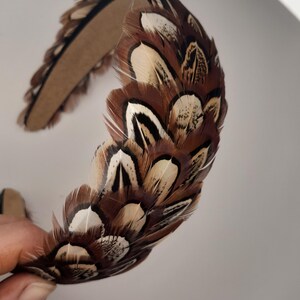 May include: A decorative headband featuring a brown and white feather design. The feathers are arranged in a layered pattern, creating a textured and eye-catching accessory. The headband is made of a sturdy material and is suitable for special occasions or everyday wear.