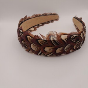 May include: A brown and cream-colored feather headband. The feathers are arranged around a brown band. The headband is a hair accessory, likely for special occasions or costume use. The feathers have a natural, textured appearance.