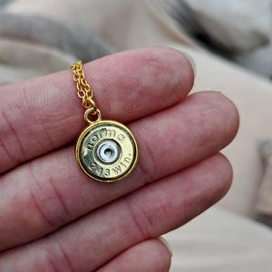 Könnte beinhalten: Eine goldfarbene Halskette mit einem Anhänger aus einer Patronenhülse. Der Anhänger trägt die Gravur "norma" und "243 Win". Die Kette ist filigran und ebenfalls goldfarben.