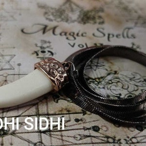 May include: A white tooth pendant with a gold-toned setting hangs from a silver chain necklace. The necklace is on a background with the words "Magic Spells" and a star of David.