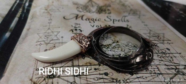 May include: A white tooth pendant with a gold-toned setting hangs from a silver chain necklace. The necklace is on a background with the words "Magic Spells" and a star of David.