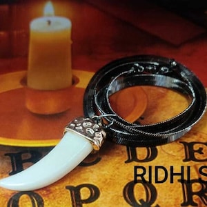 May include: A white fang pendant necklace with a silver chain. The pendant is on a black and gold Ouija board with the letters A, B, C, D, E, F, G, R, I, D, H, L, S, I, D, H, L, Q, R, S.