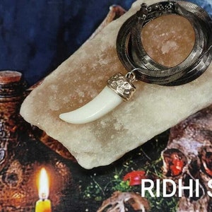 May include: A white tooth pendant on a silver chain necklace. The pendant is on a white rock with a silver chain wrapped around it. The background is a dark blue surface with candles and a skull.