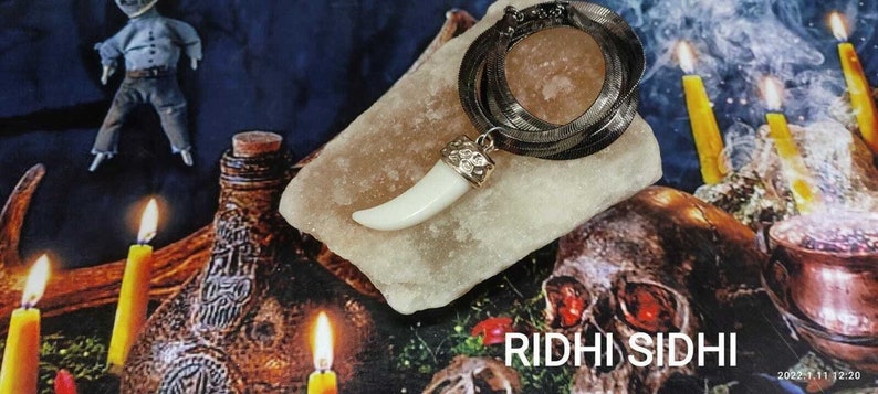 May include: A white tooth pendant on a silver chain necklace. The pendant is on a white rock with a silver chain wrapped around it. The background is a dark blue surface with candles and a skull.