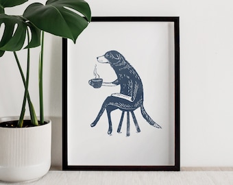 May include: A blue and white illustration of a dog sitting on a stool and holding a cup of coffee. The dog is drawn in a simple, stylized manner. The illustration is framed in a black frame.