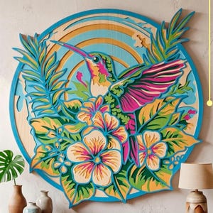 May include: A circular multi-layered wooden wall art piece featuring a hummingbird surrounded by tropical flowers and leaves in shades of pink, green, blue, and yellow. The design includes text on the right reading DXF AI SVG and at the bottom DIGITAL CUTTING FILE.