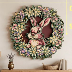 May include: A multi-layered wall art piece featuring a central rabbit surrounded by a circular wreath of flowers in shades of pink, green, and cream. The design includes text on the right side reading DXF, AI, and SVG, indicating a digital file.