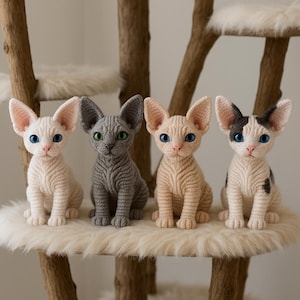 Puede incluir: Cuatro figuras de gatos Sphynx de ganchillo en tonos crema, gris y beige, con orejas grandes y ojos azules o verdes. Se encuentran sobre una superficie blanca y esponjosa, parte de una estructura de árbol para gatos.