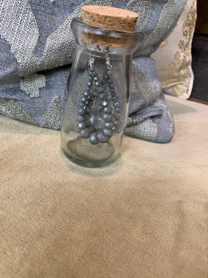 May include: Gray crystal beaded dangle earrings in a clear glass bottle with a cork top.