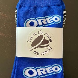May include: Blue socks with the Oreo logo in white and light blue. A white sticker wraps around the socks with the text "You're the cream to my cookie!" in a circular design.