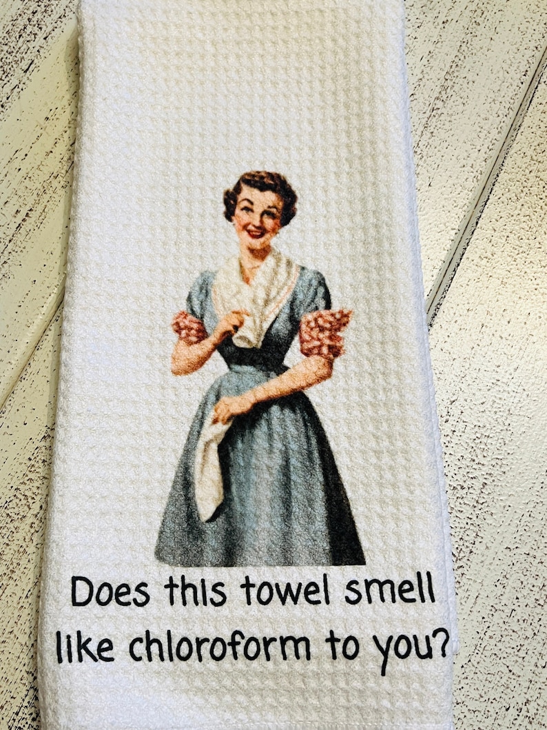 K&ouml;nnte beinhalten: Ein wei&szlig;es K&uuml;chentuch mit einer Vintage-Illustration einer Frau, die ein Handtuch h&auml;lt. Der Text auf dem Handtuch lautet "Riecht dieses Handtuch nach Chloroform?"