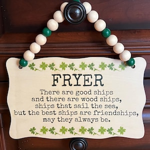 May include: Wooden sign with the name "FRYER" in bold letters, featuring a quote about friendships. The sign is decorated with shamrock designs and a beaded hanger with green and natural-toned beads.