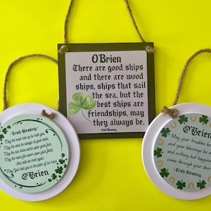 May include: Three St. Patrick's Day themed hanging decorations. Two are round with Irish blessings and shamrock designs. The third is square with a quote about friendship and a shamrock. All have the name "O'Brien".