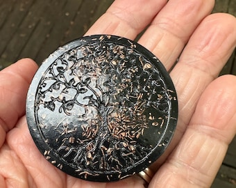 Peut inclure: Un disque noir circulaire présentant un motif d'arbre de vie en relief avec une finition en cuivre métallique. Le motif de l'arbre couvre toute la surface, affichant des branches et des racines complexes contrastant avec le fond noir lisse.