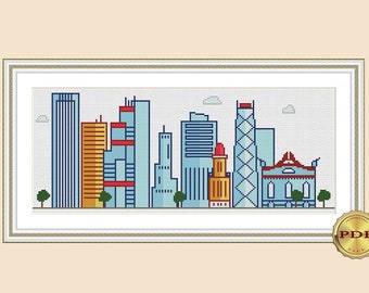 May include: A cross-stitch pattern of a city skyline with buildings in various colors, including blue, red, yellow, and green. The buildings are arranged in a row, with the tallest building in the center. The pattern is framed in a light brown frame.