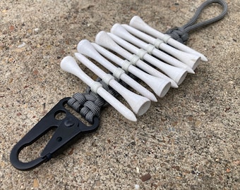 May include: A black carabiner clip attached to a gray paracord lanyard with a series of white golf tees tied to it.