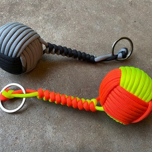 May include: Two handmade keychains with knotted balls. One keychain has a gray and black ball, the other has a yellow and orange ball.