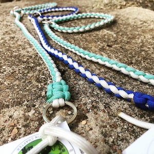 May include: Three braided ropes in white, blue, and teal colors. The ropes are tied together with a knot at the end and have a silver ring attached.