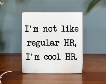 May include: White wooden block sign with black text that reads "I'm not like regular HR, I'm cool HR."