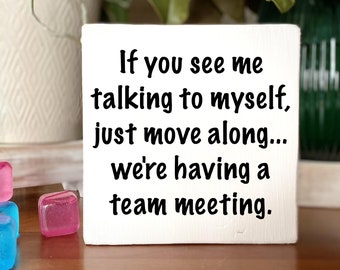 May include: White wooden sign with black text that reads "If you see me talking to myself, just move along... we're having a team meeting."