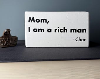 Divertido letrero de madera de granja con frase "Mamá, soy un hombre rico" y cita de Cher.