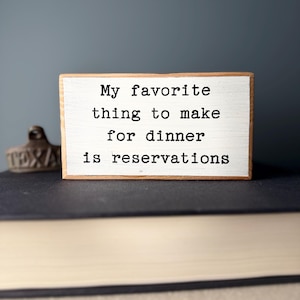 May include: White wooden sign with black text that reads "My favorite thing to make for dinner is reservations".
