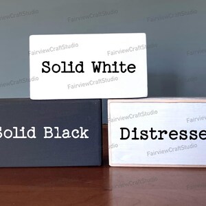 Puede incluir: Tres bloques de madera con diferentes acabados de pintura. El bloque superior es blanco con texto negro que dice "Solid White". El bloque del medio es negro con texto blanco que dice "Solid Black". El bloque inferior es blanco con texto negro que dice "Distressed".