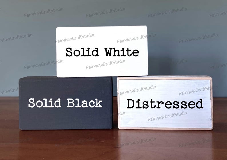Puede incluir: Tres bloques de madera con diferentes acabados de pintura. El bloque superior es blanco con texto negro que dice "Solid White". El bloque del medio es negro con texto blanco que dice "Solid Black". El bloque inferior es blanco con texto negro que dice "Distressed".