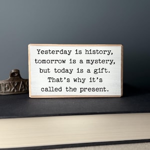 May include: A wooden sign with the text "Yesterday is history, tomorrow is a mystery, but today is a gift. That's why it's called the present."