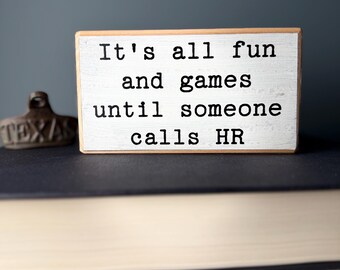May include: White wooden sign with black text that reads "It's all fun and games until someone calls HR".