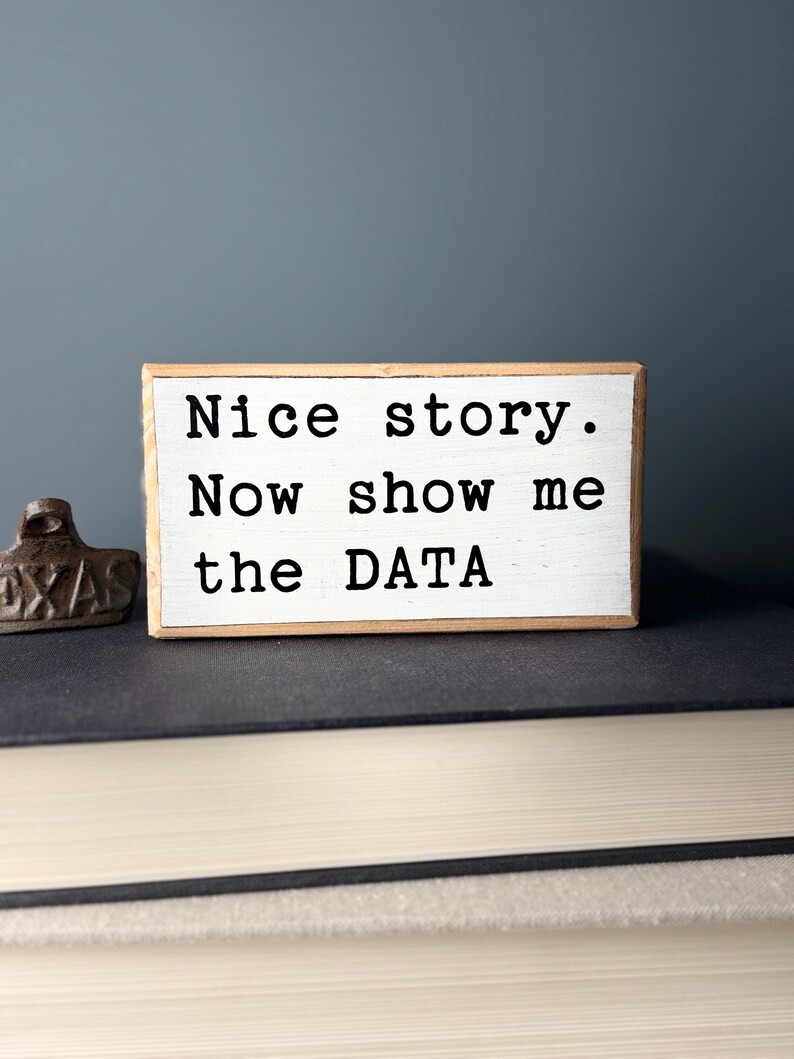 May include: White wooden block with the text "Nice story. Now show me the DATA" in black lettering.
