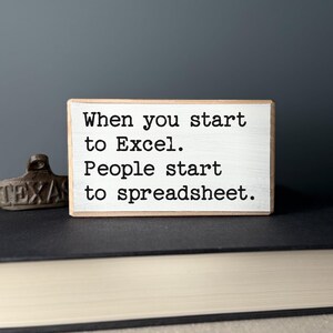 K&ouml;nnte beinhalten: Ein wei&szlig;es Holzschild mit schwarzem Text, der lautet: "When you start to Excel. People start to spreadsheet."