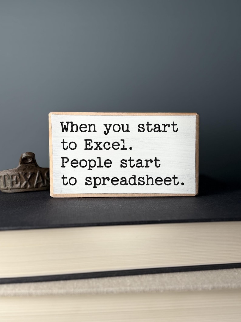 K&ouml;nnte beinhalten: Ein wei&szlig;es Holzschild mit schwarzem Text, der lautet: "When you start to Excel. People start to spreadsheet."
