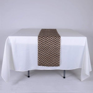May include: A brown and black chevron patterned burlap table runner on a white tablecloth.