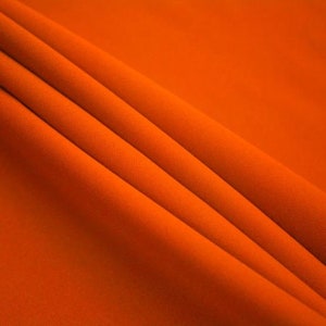 May include: Close-up of a smooth, orange fabric with soft folds and wrinkles. The fabric has a subtle sheen and a slightly textured surface.