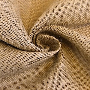 May include: A close-up of a natural brown burlap fabric with a rough texture. The fabric is folded and draped, showing the weave and the natural fibers.