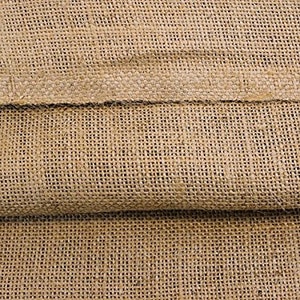 May include: Close-up of a natural brown burlap fabric with a woven texture. The fabric is folded in half, showing the two layers.