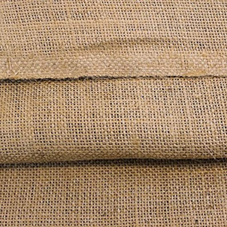 May include: Close-up of a natural brown burlap fabric with a woven texture. The fabric is folded in half, showing the two layers.