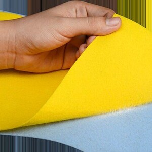 Puede incluir: Una hoja de fieltro amarillo se est&aacute; despegando para revelar una hoja de fieltro azul claro debajo.