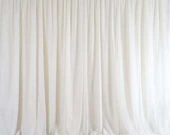 May include: A white sheer backdrop curtain with a gathered top edge. The curtain is made of a lightweight fabric and has a soft, flowing drape.